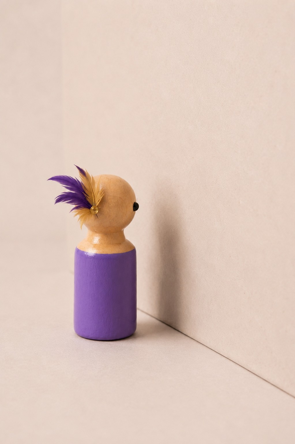 Boneco roxo com penas em um canto silencioso — quem ainda não foi visto.